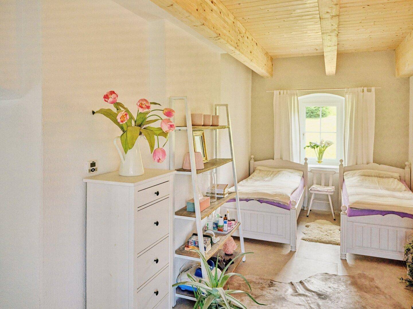 Kinder- oder Gästezimmer mit zwei Einzelbetten, Holzbalkendecke und hellem Ambiente.