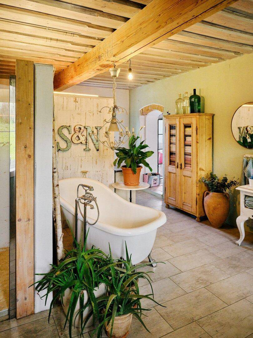 Badezimmer mit freistehender Badewanne, Holzbalkendecke und Pflanzen für eine entspannte Atmosphäre.