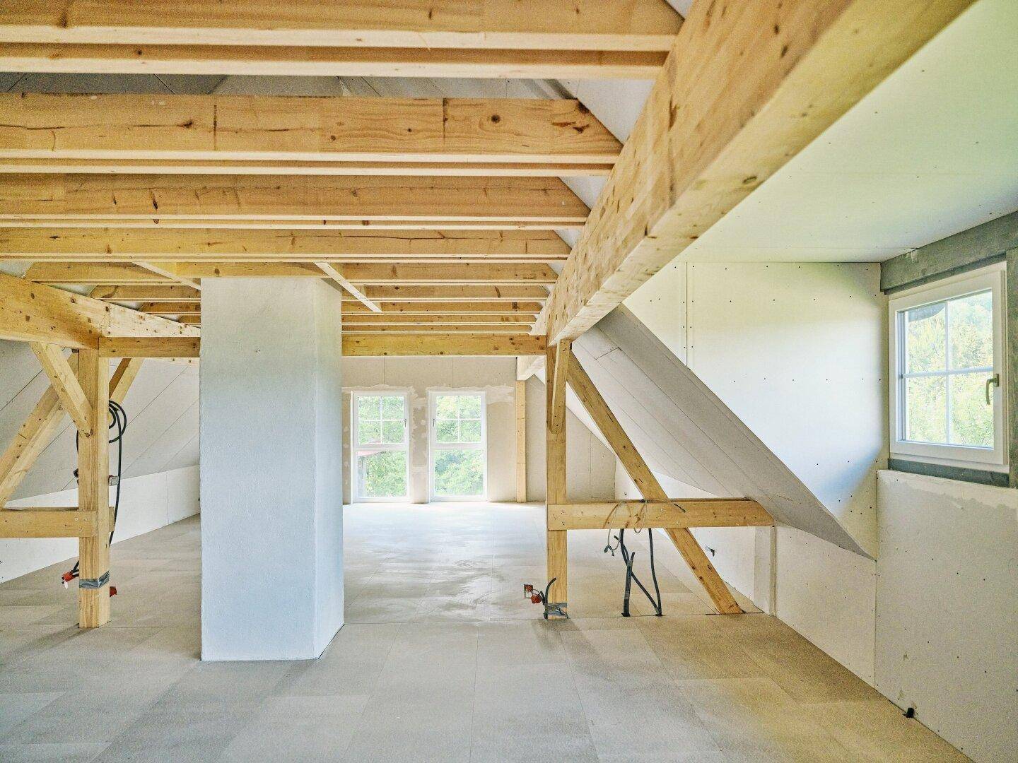 Geräumiger Dachboden im Rohbau mit sichtbaren Holzbalken und Fenstern, bereit für den Ausbau.