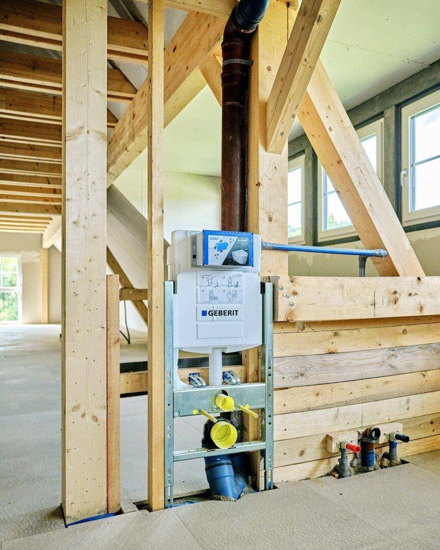 Installation eines Geberit WC-Systems im Rohbau des Dachbodens, umgeben von Holzbalken.