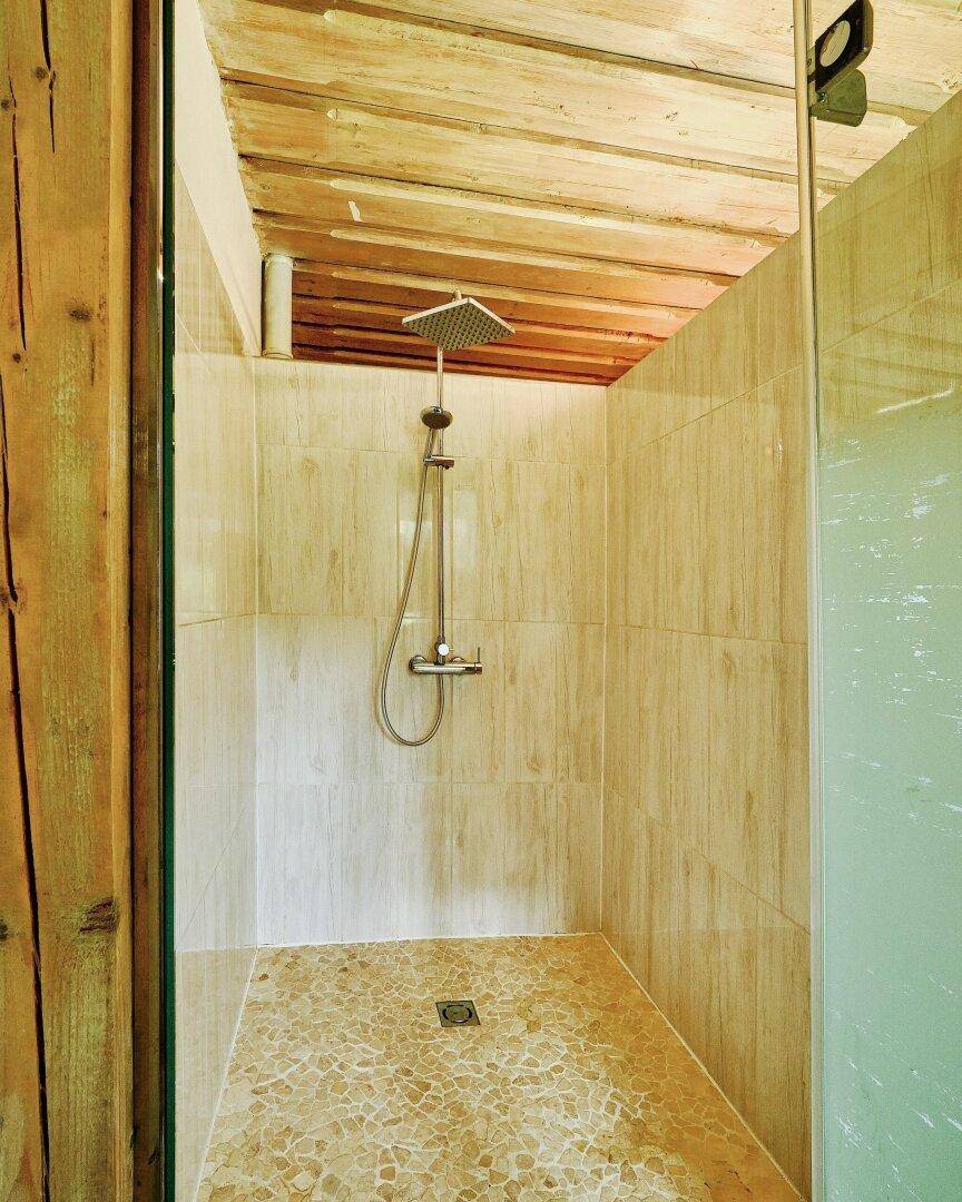 Duschbereich mit gefliesten Wänden, Kieselsteinboden und einer Holzdecke im rustikalen Stil.