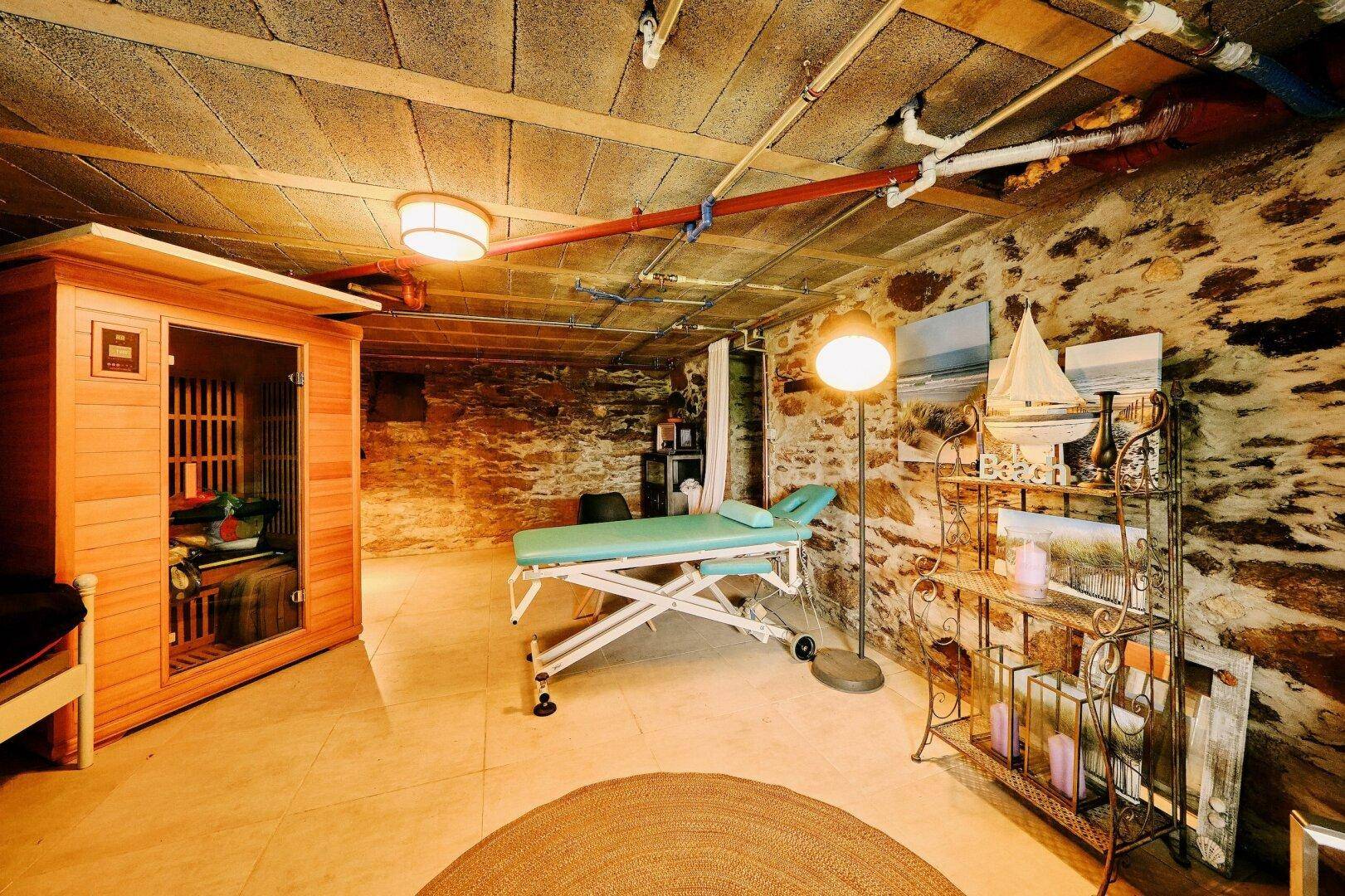Gemütlicher Kellerraum mit Natursteinwänden, ausgestattet mit einer Sauna und einer Massageliege.