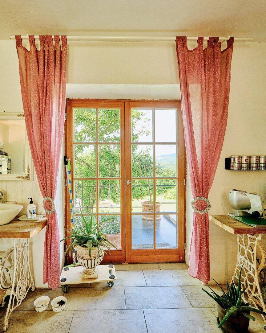 Große Fenstertür in der Küche mit Blick ins Grüne und rosa Vorhängen.