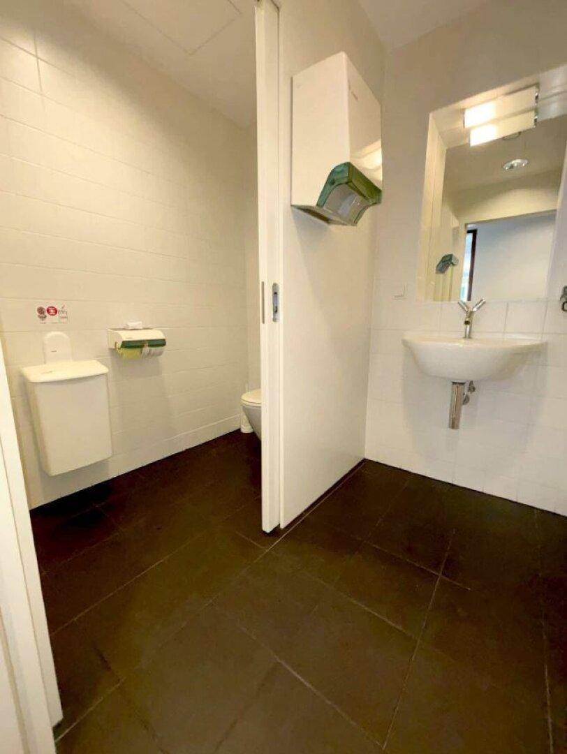 Saubere und funktionale Toilette mit weißen Fliesen, Waschbecken und einem Handtrockner an der Wand.