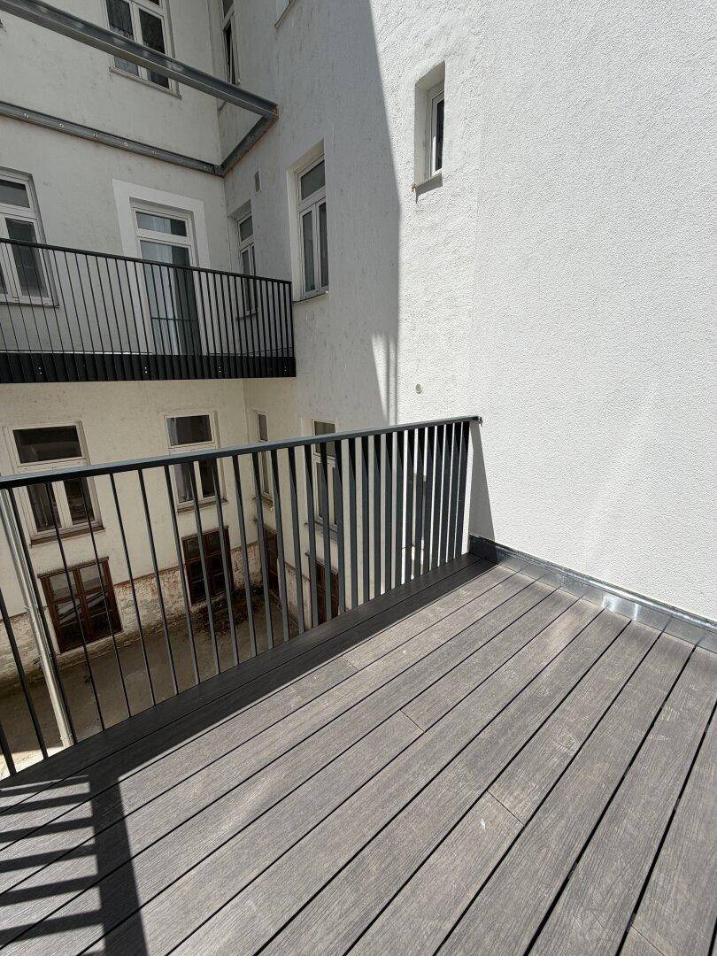 Balkon mit Holzbelag und Metallgeländer, der einen Blick auf den Innenhof bietet.