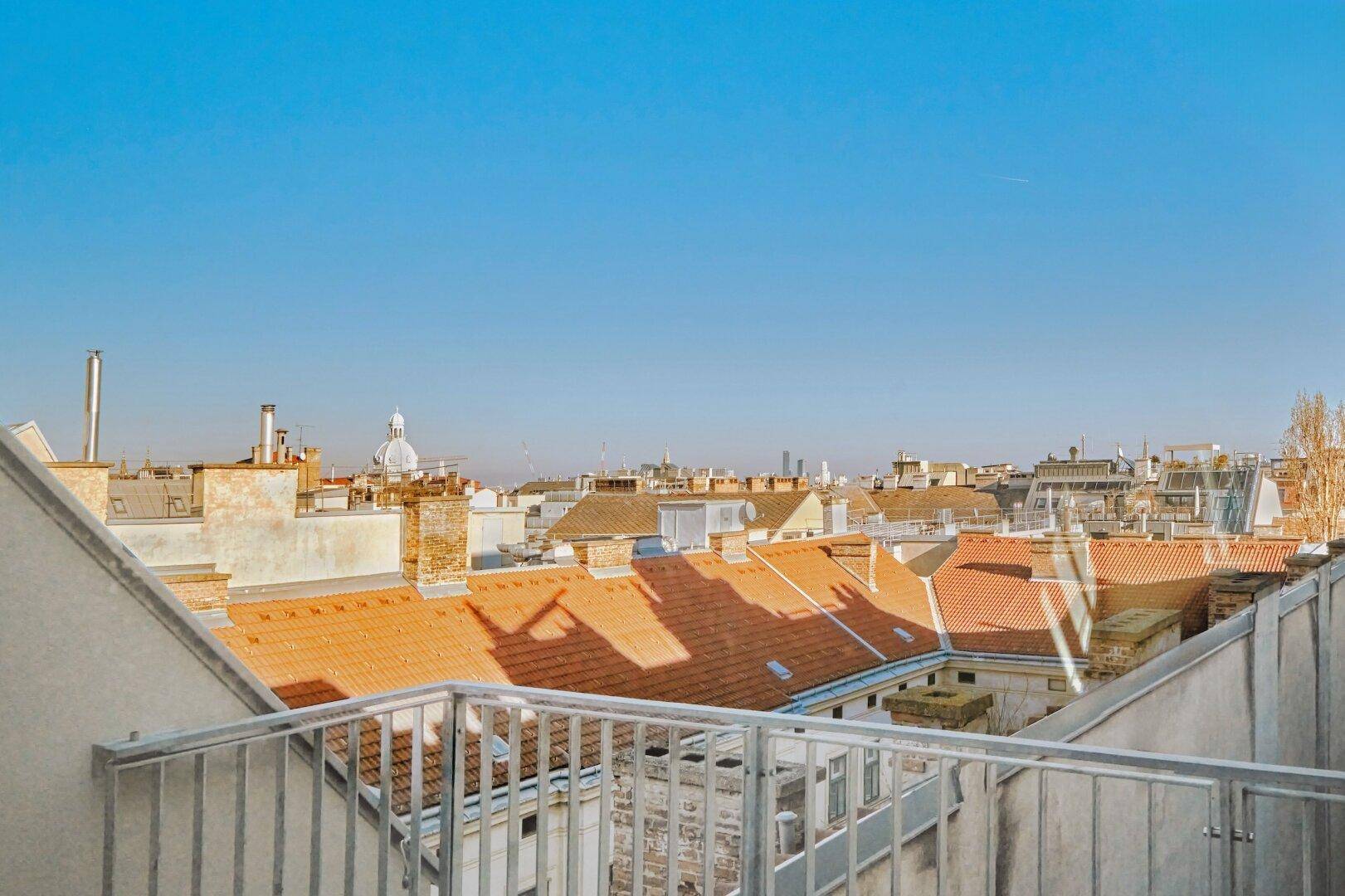 Weitläufiger Blick über die Dächer der Stadt mit traditionellen Ziegeldächern unter blauem Himmel.