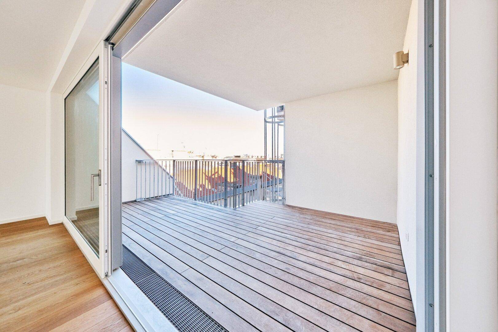 Großer Balkon mit Holzbelag und Metallgeländer, bietet einen weiten Blick über die Stadt.