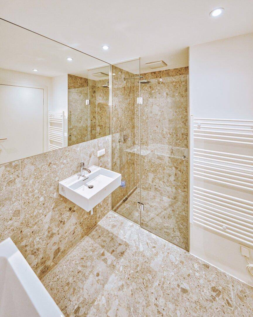 Modernes Badezimmer mit begehbarer Dusche, großem Spiegel und Natursteinfliesen in neuwertigem Zustand.