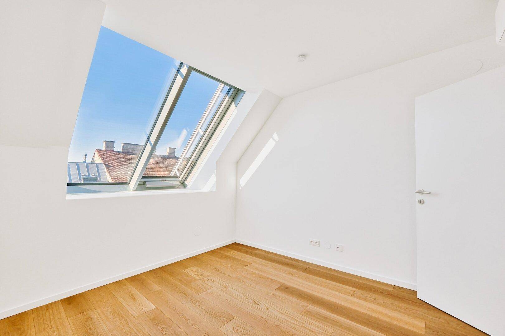 Helles Dachzimmer mit Holzboden, schrägen Wänden und großem Dachfenster in neuwertigem Zustand.