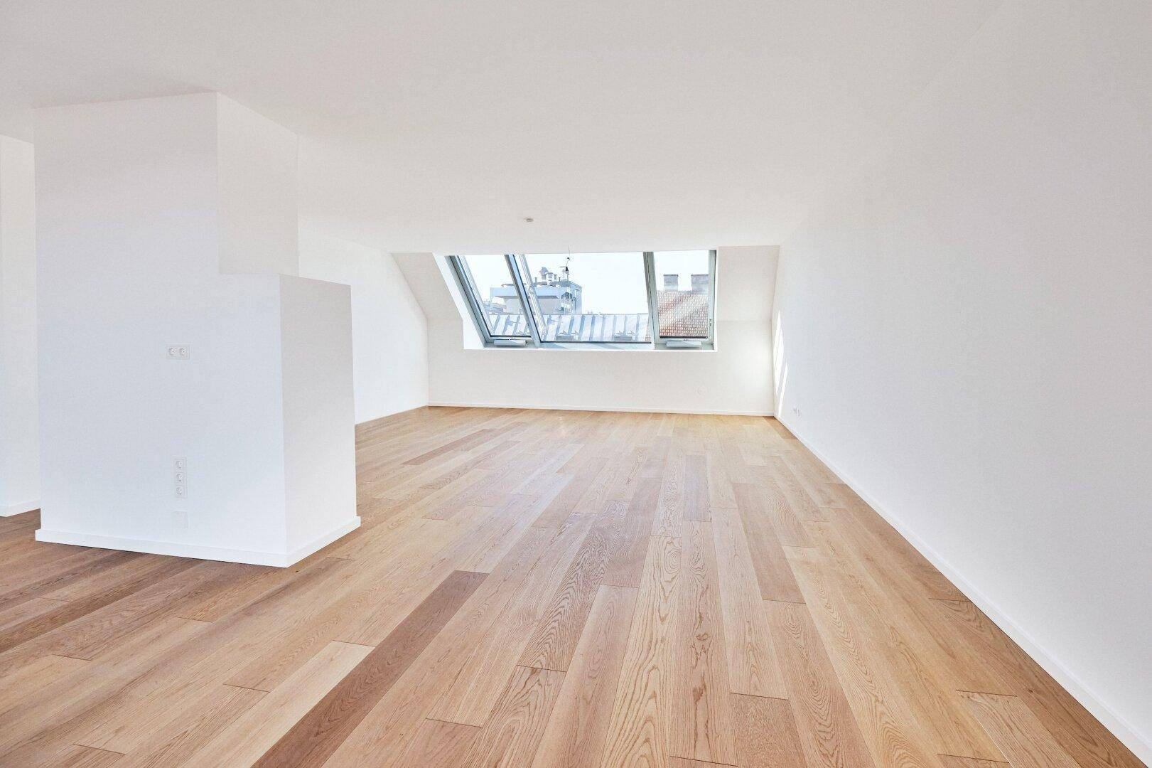Heller Raum im Dachgeschoss mit Holzboden, Dachfenster und schrägen Wänden in neuwertigem Zustand.