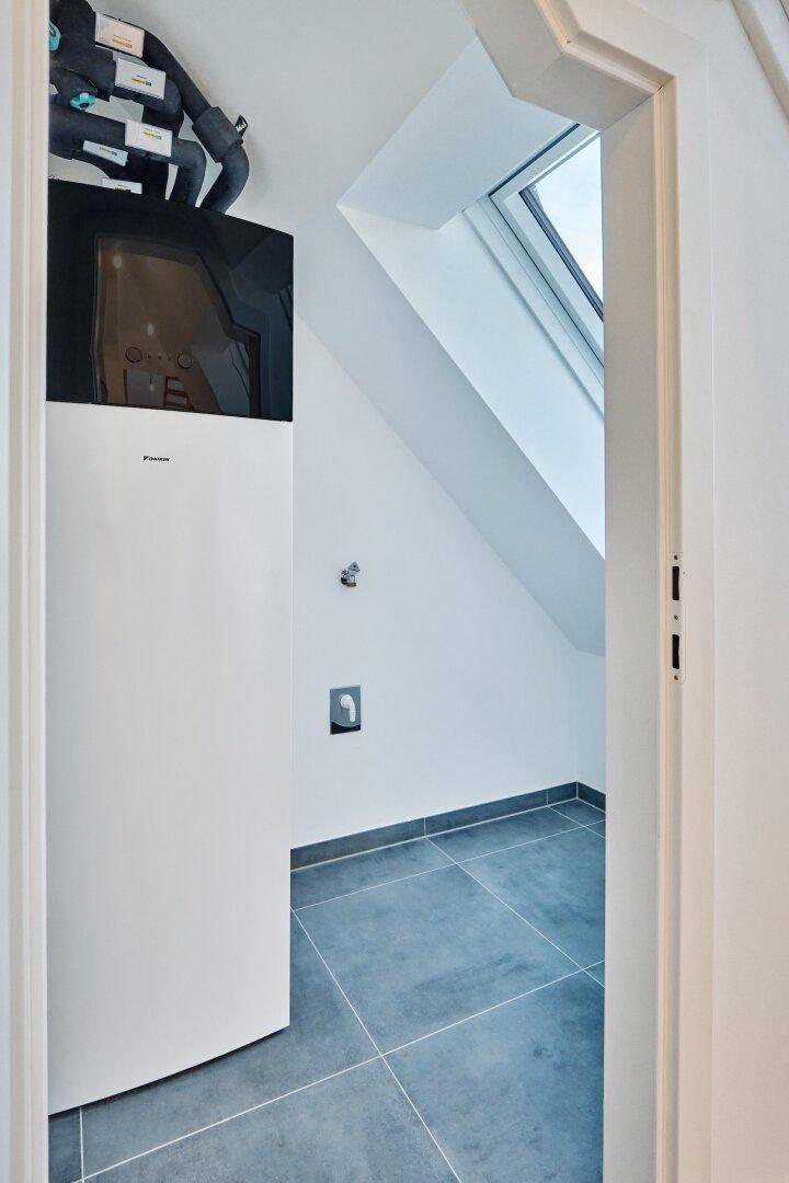 Technikraum mit Wärmepumpe und Rohrleitungen, unter einem Dachfenster gelegen.