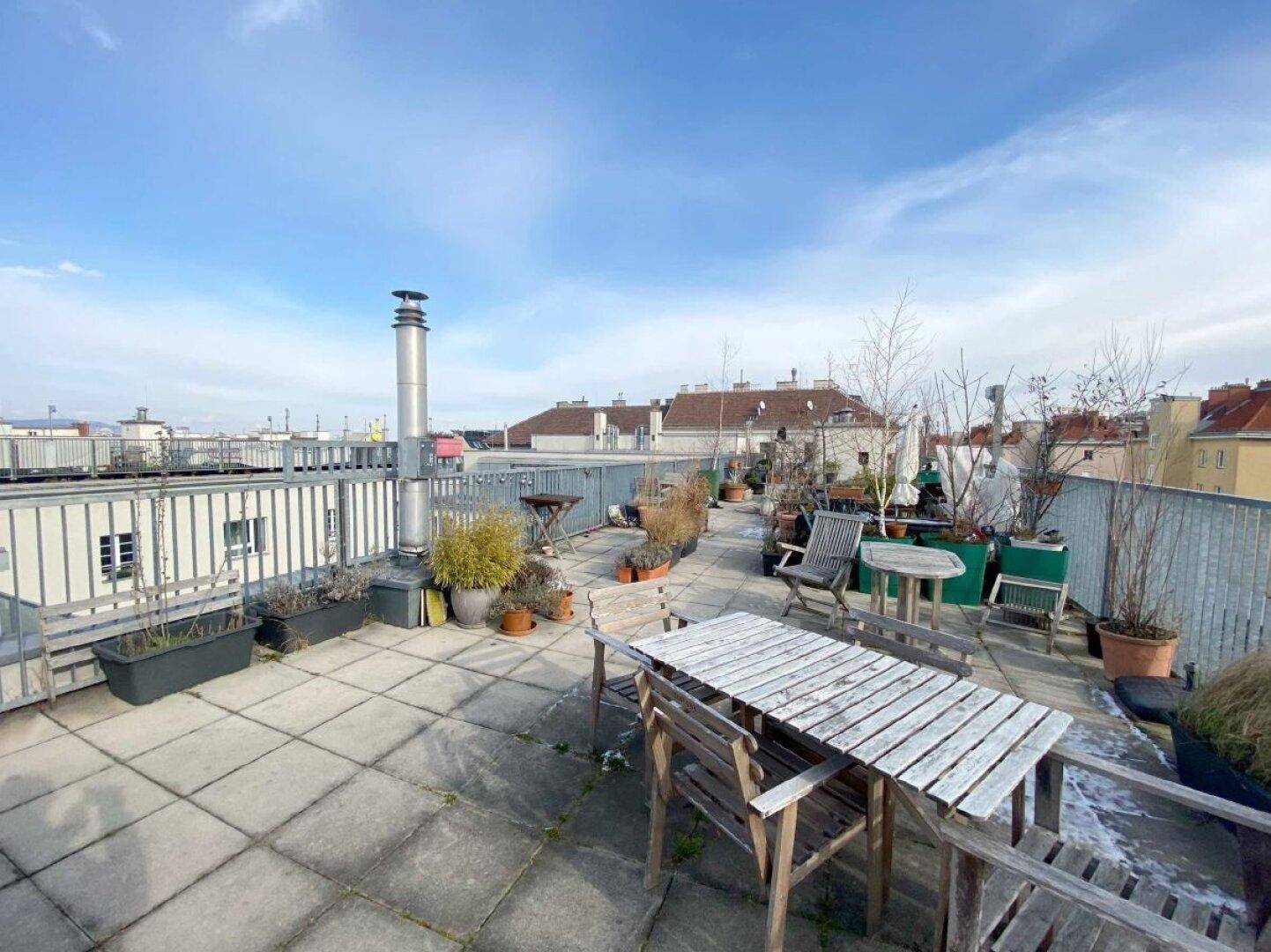 Weitläufige Dachterrasse mit Stadtblick, Sitzgelegenheiten und Pflanzen in Töpfen.