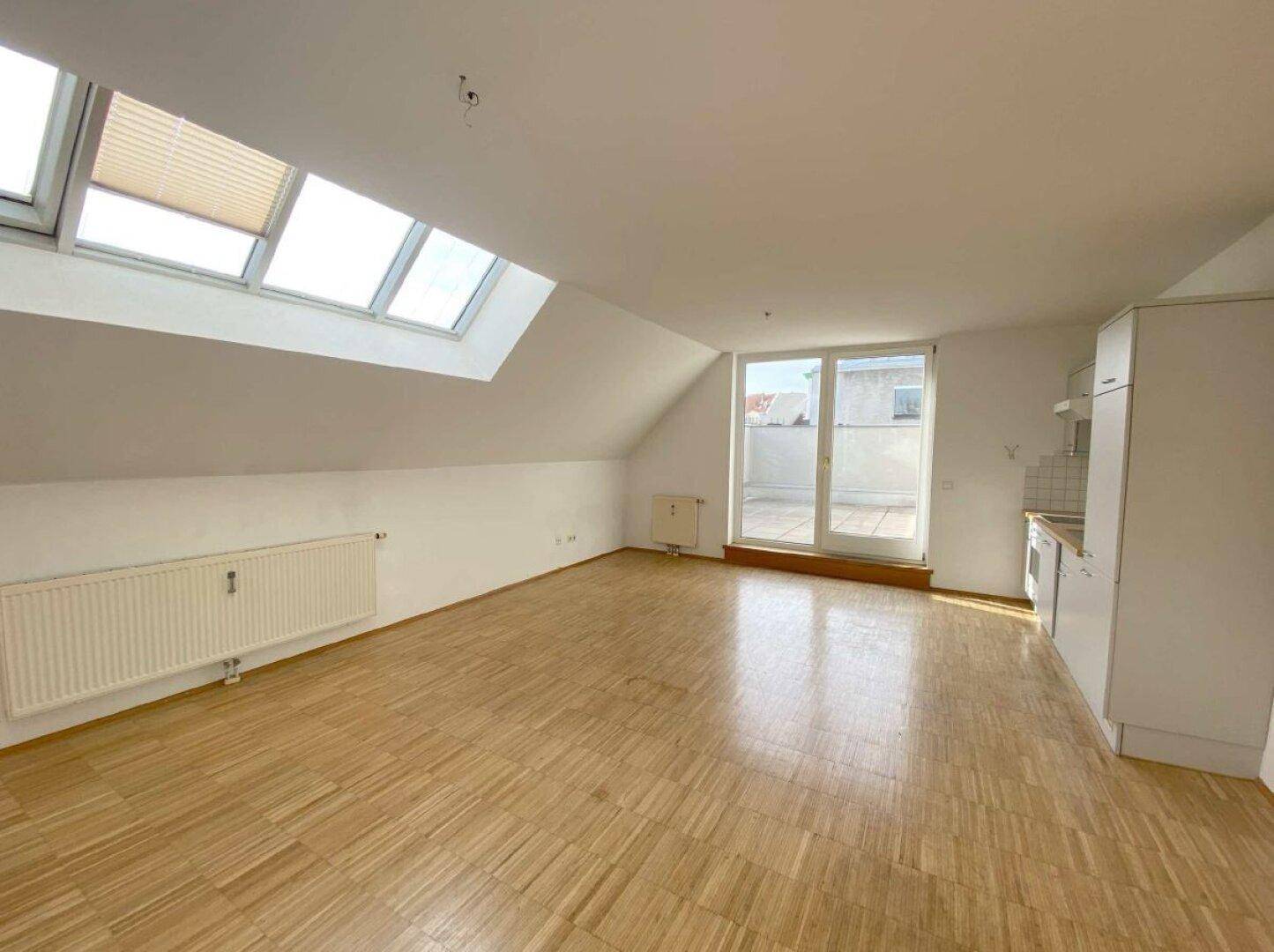 Lichtdurchfluteter Wohnbereich mit Holzboden, Dachfenstern und Zugang zur Dachterrasse.