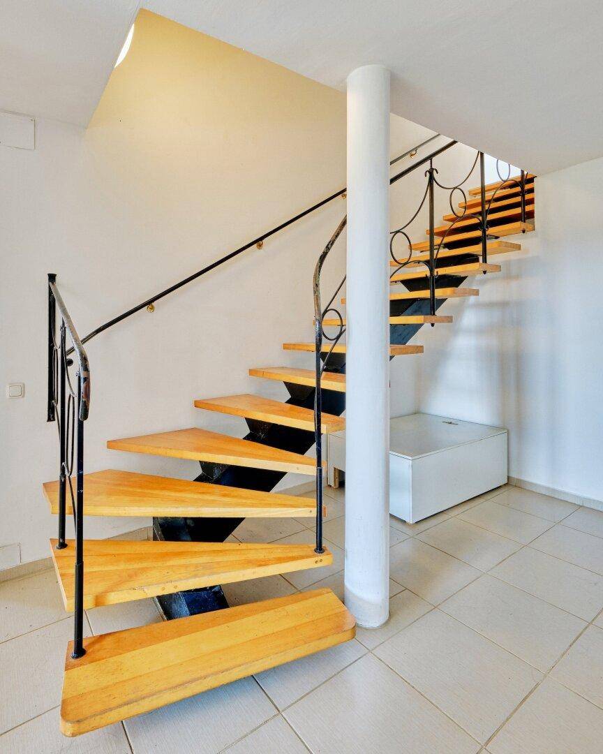Elegante Wendeltreppe aus Holz mit schmiedeeisernem Geländer in einem hellen Eingangsbereich.