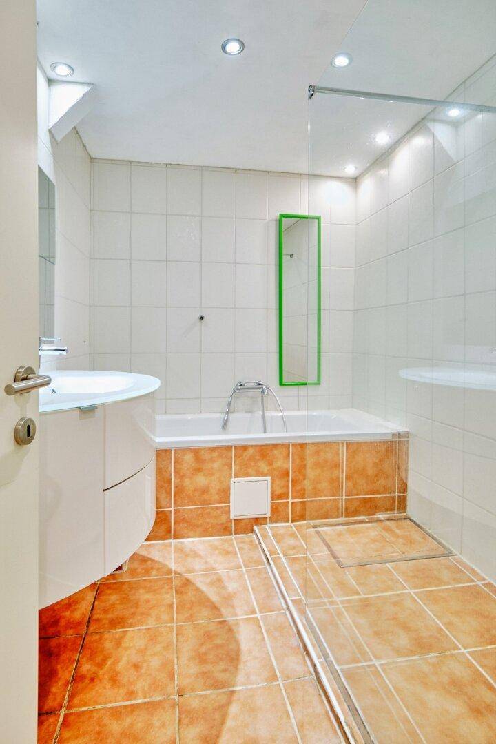Badezimmer mit Badewanne, Waschbecken und terracottafarbenen Fliesen, hell beleuchtet.