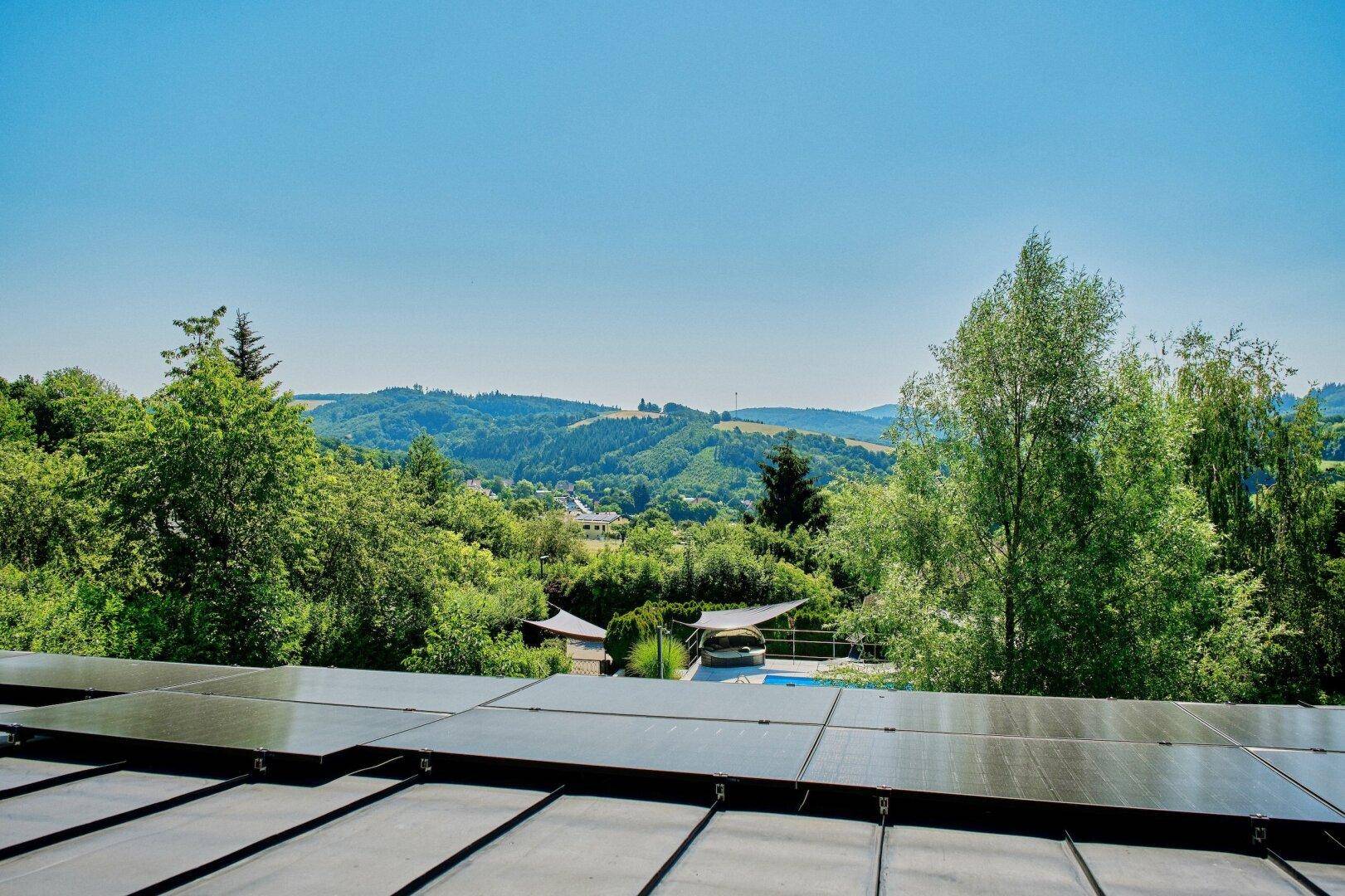 Dachfläche mit Photovoltaikanlage und weitem Blick über die grüne Hügellandschaft.