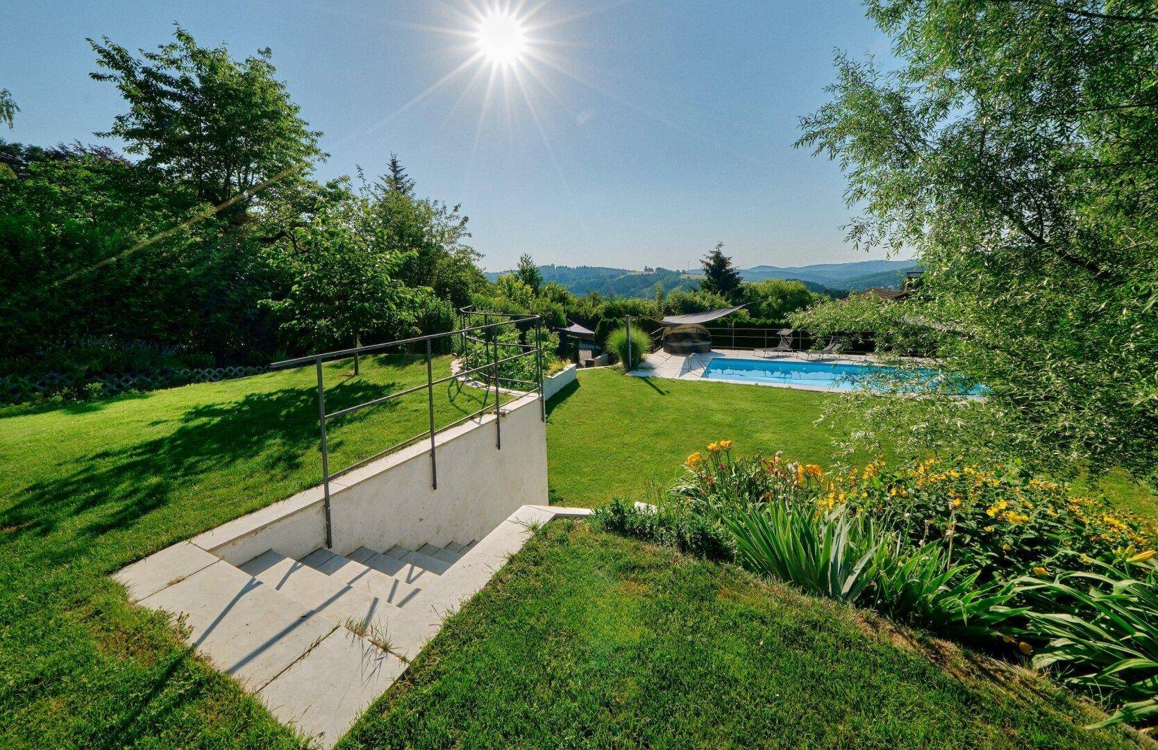 Weitläufiger Garten mit Treppen, Rasenflächen und Fernblick auf die umliegende Hügellandschaft und den Pool.