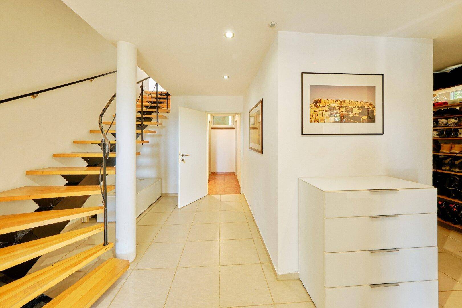 Geräumiger Flur mit heller Fliese, offener Holztreppe und Blick auf weitere Zimmer.