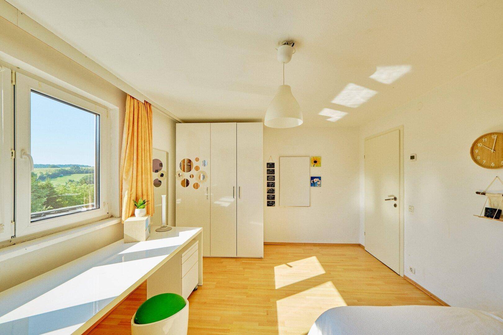 Helles Schlafzimmer mit Holzboden, Schreibtisch und Kleiderschrank, sonnendurchflutet.