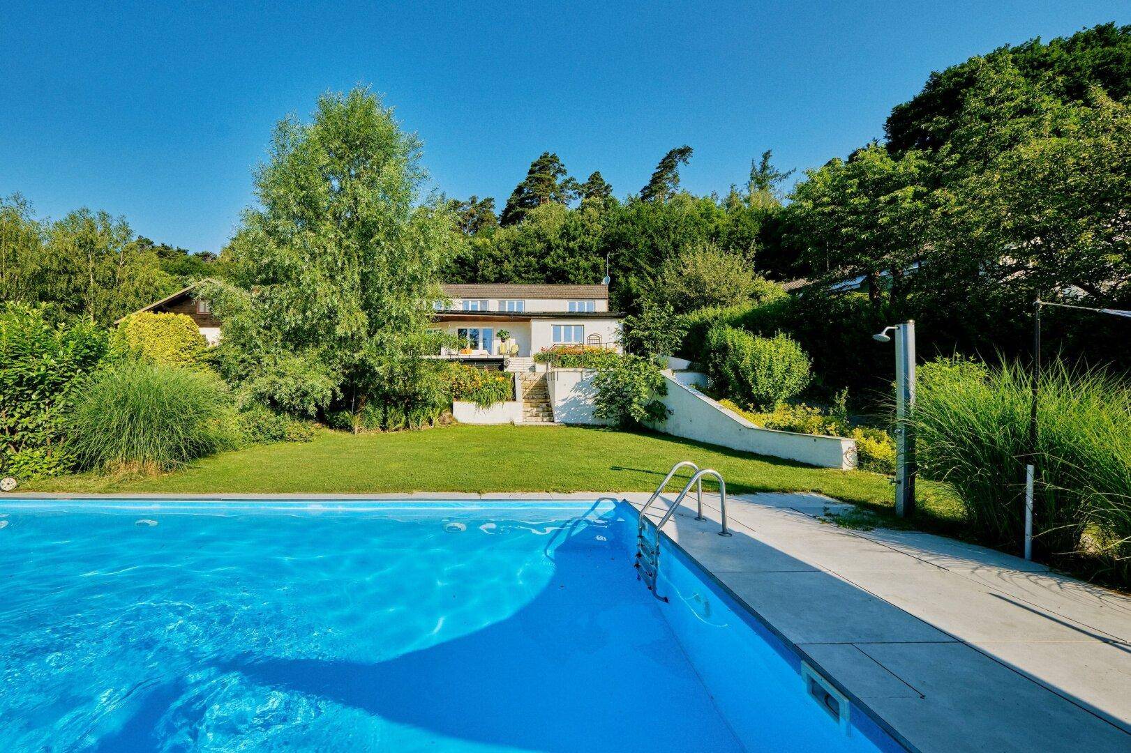Großzügiger Außenbereich mit Schwimmbad und Blick auf das moderne Haus und die grüne Landschaft.