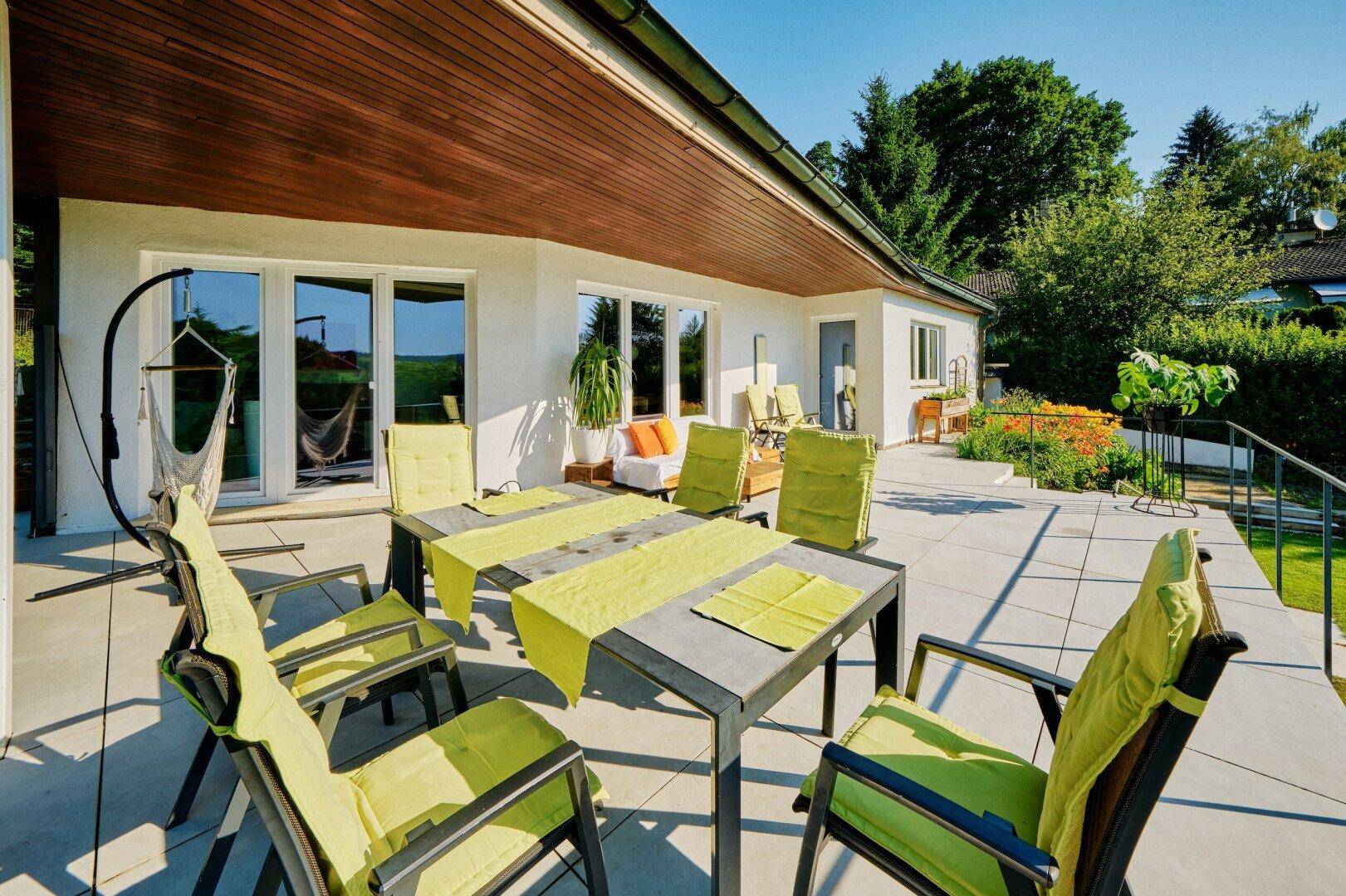 Helle Terrasse mit Essgruppe, Hängematte und Zugang zum Garten, umgeben von viel Grün.