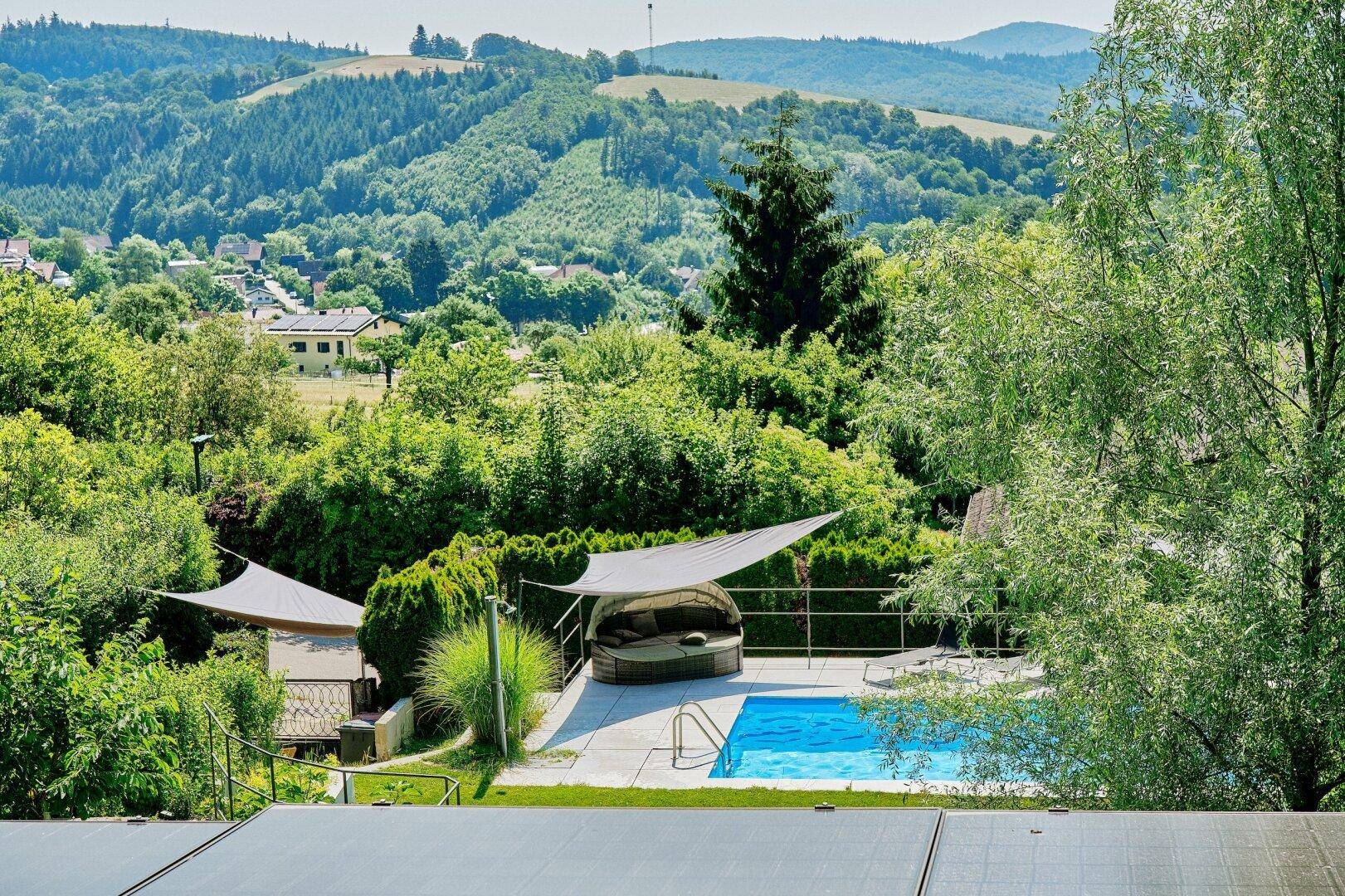 Panoramablick auf den Poolbereich mit Liegemöbeln und die weite, grüne Hügellandschaft.