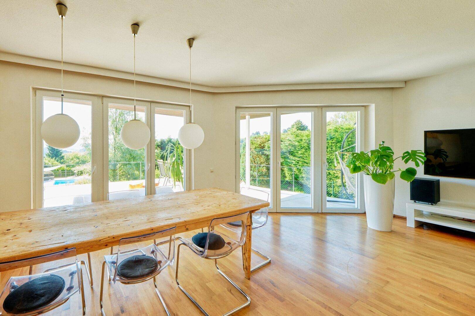 Heller Essbereich mit Holztisch, modernen Stühlen und großen Fenstern mit Zugang zur Terrasse.
