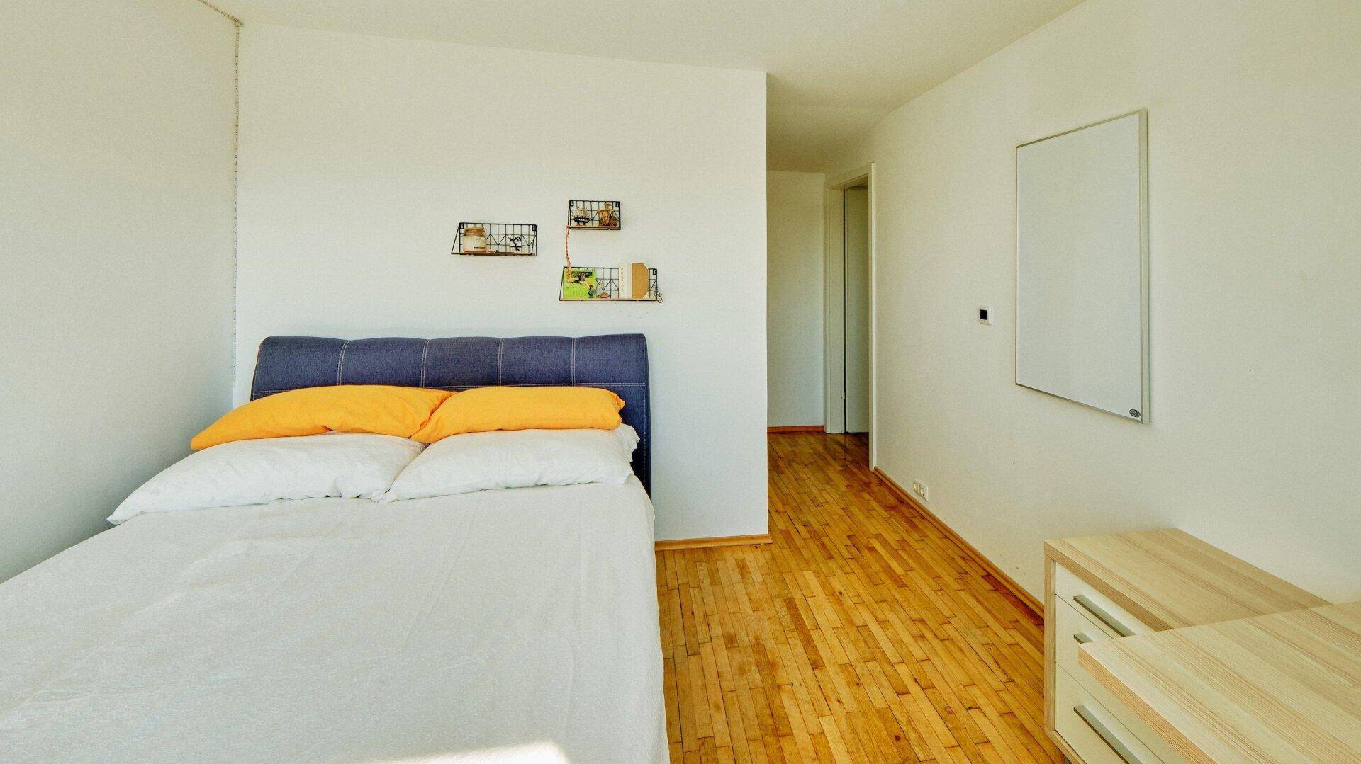 Schlafzimmer mit Holzboden, Doppelbett und schlichten Möbeln in hellem Ambiente.