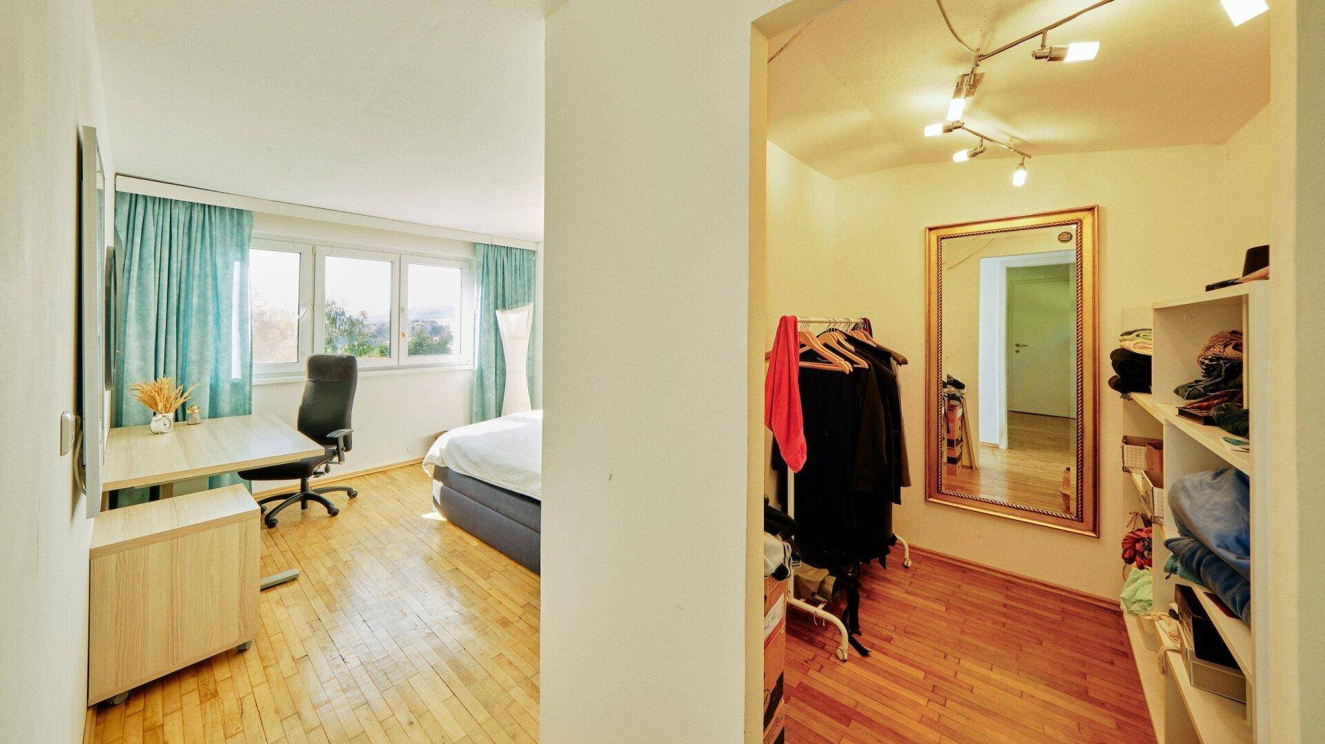 Schlafzimmer mit Holzboden und angrenzendem begehbarem Kleiderschrank mit großem Spiegel.