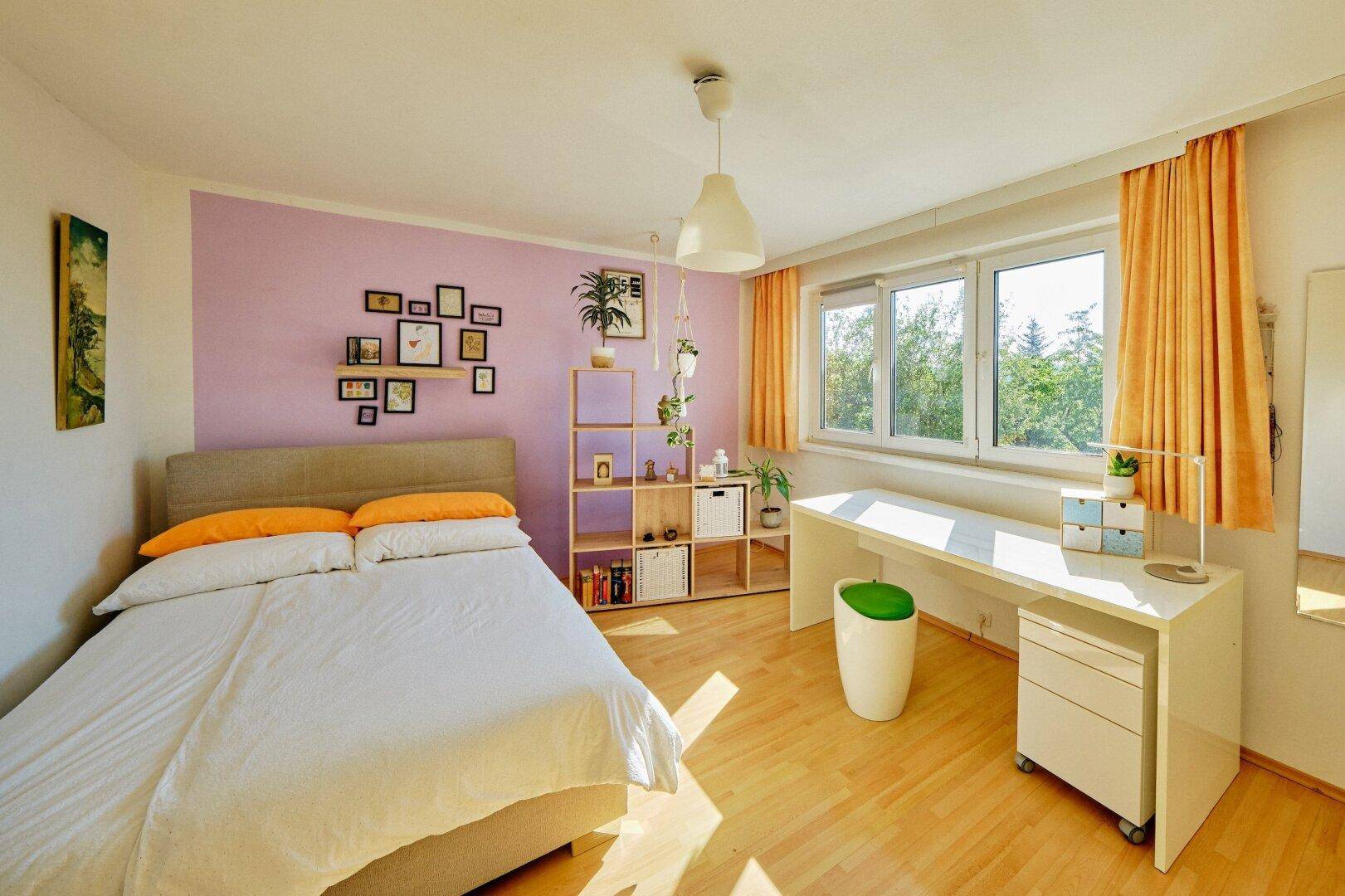 Helles Schlafzimmer mit Holzboden, Schreibtisch und farbiger Wandgestaltung.