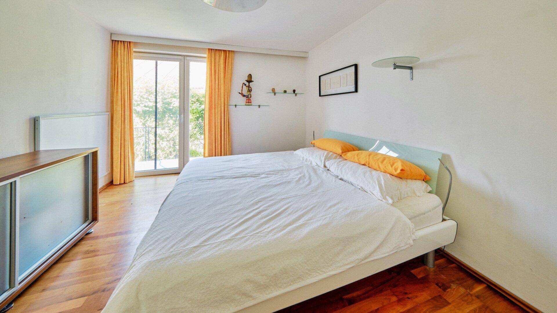 Schlafzimmer mit Holzboden, Doppelbett und Zugang zu einem französischen Balkon.