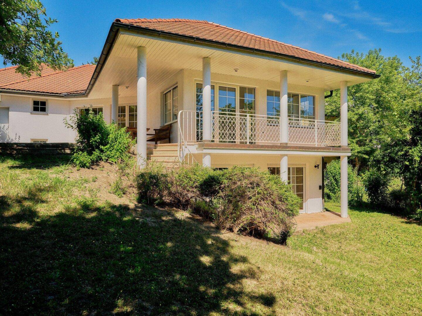 Ansicht des Hauses von der Gartenseite mit Balkon und Zugang zum Untergeschoss in sonniger Umgebung.