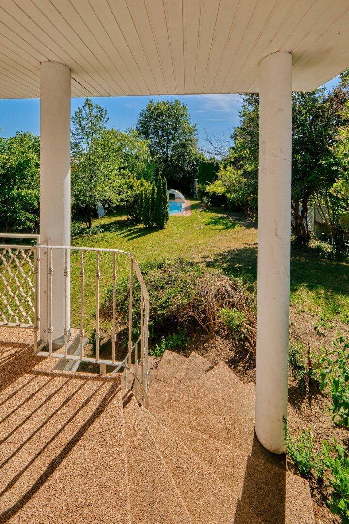 Treppe vom überdachten Balkon führt direkt in den weitläufigen Garten mit sichtbarem Pool.