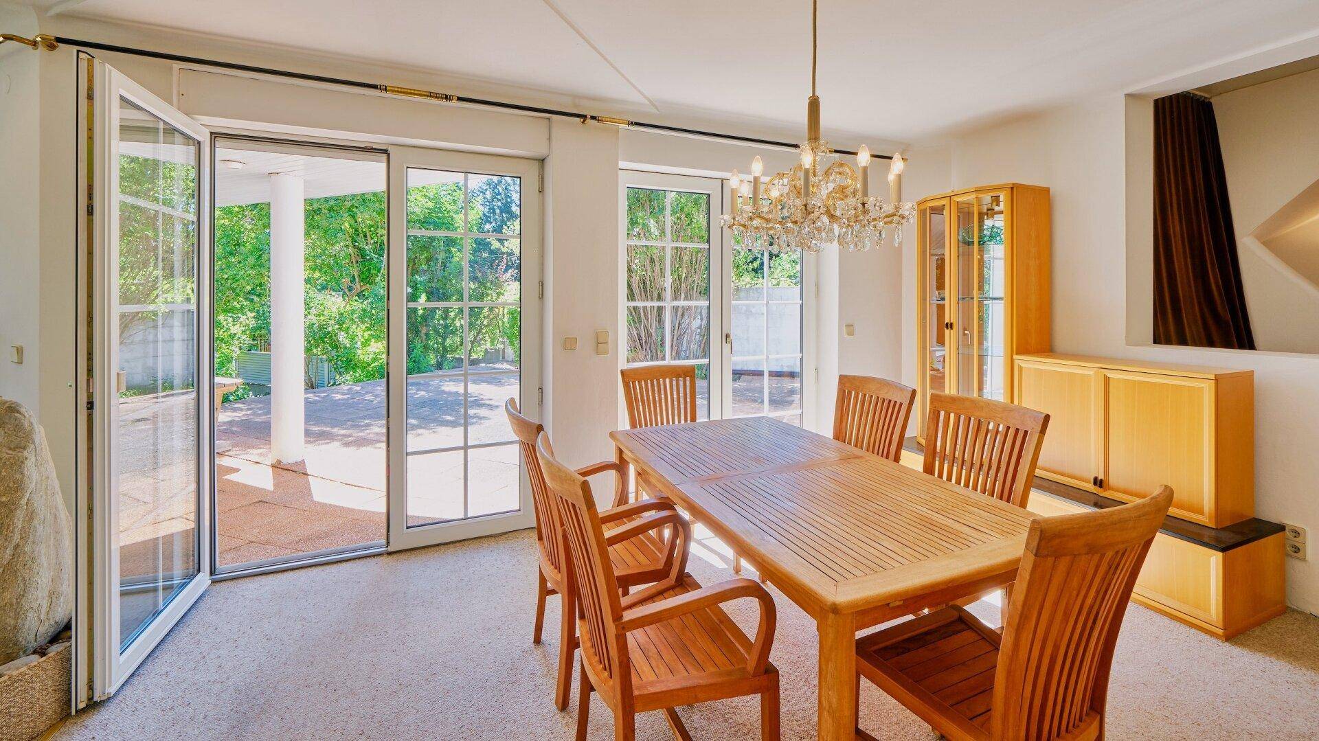 Esszimmer mit Holztisch und Stühlen, elegantem Kronleuchter und Zugang zur Terrasse.