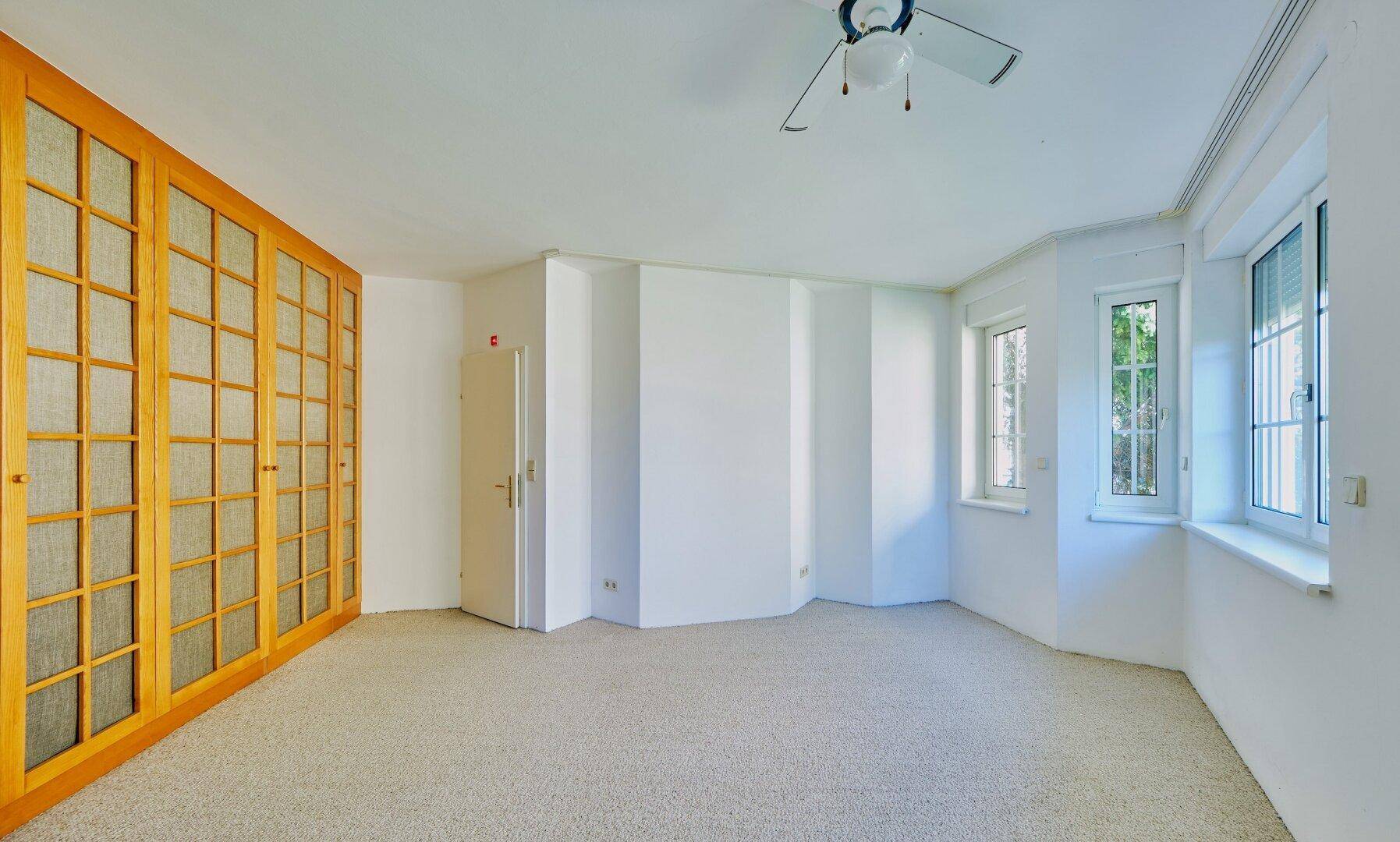 Geräumiges Schlafzimmer mit Teppichboden, Einbauschränken und Deckenventilator für Komfort.