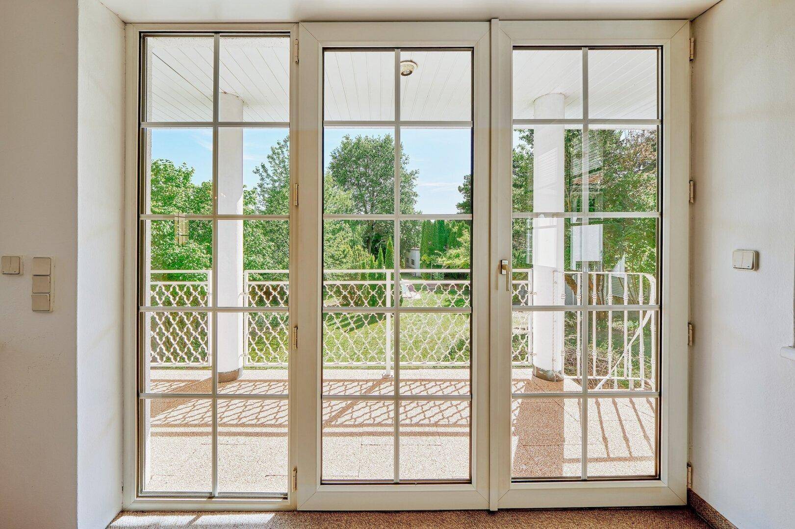Große Fenstertüren bieten einen schönen Blick auf den Balkon und den grünen Gartenbereich.