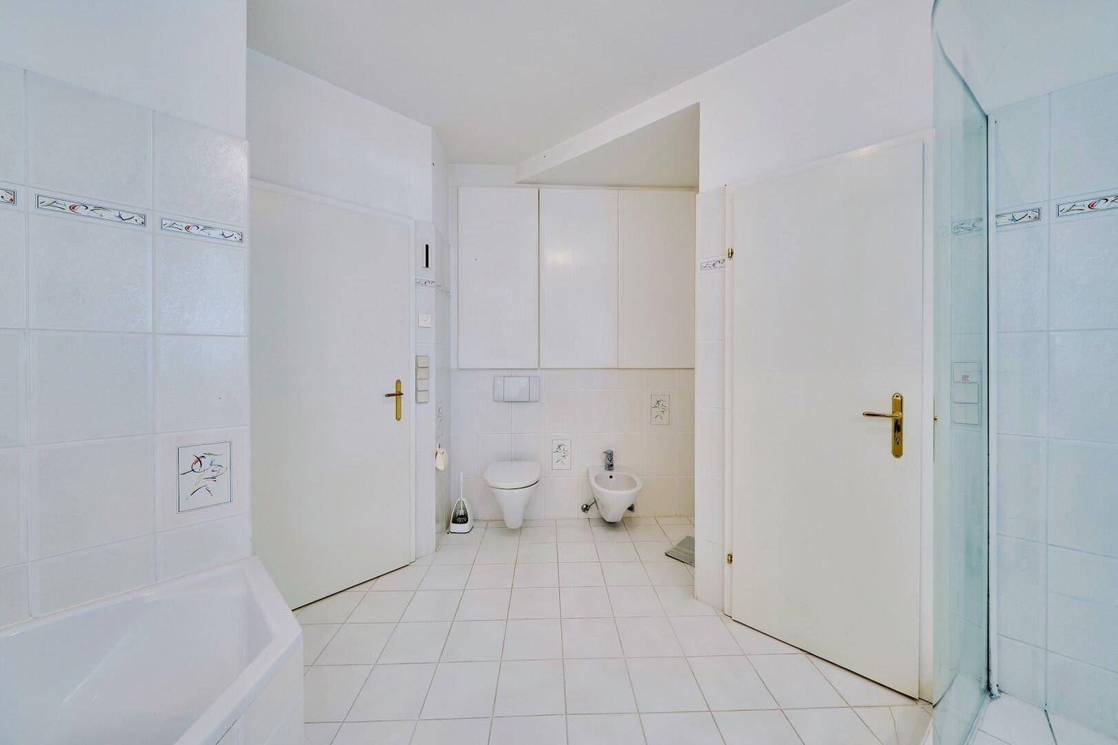 Helles Badezimmer mit weißen Fliesen, Badewanne, Dusche, WC und Bidet für volle Funktionalität.