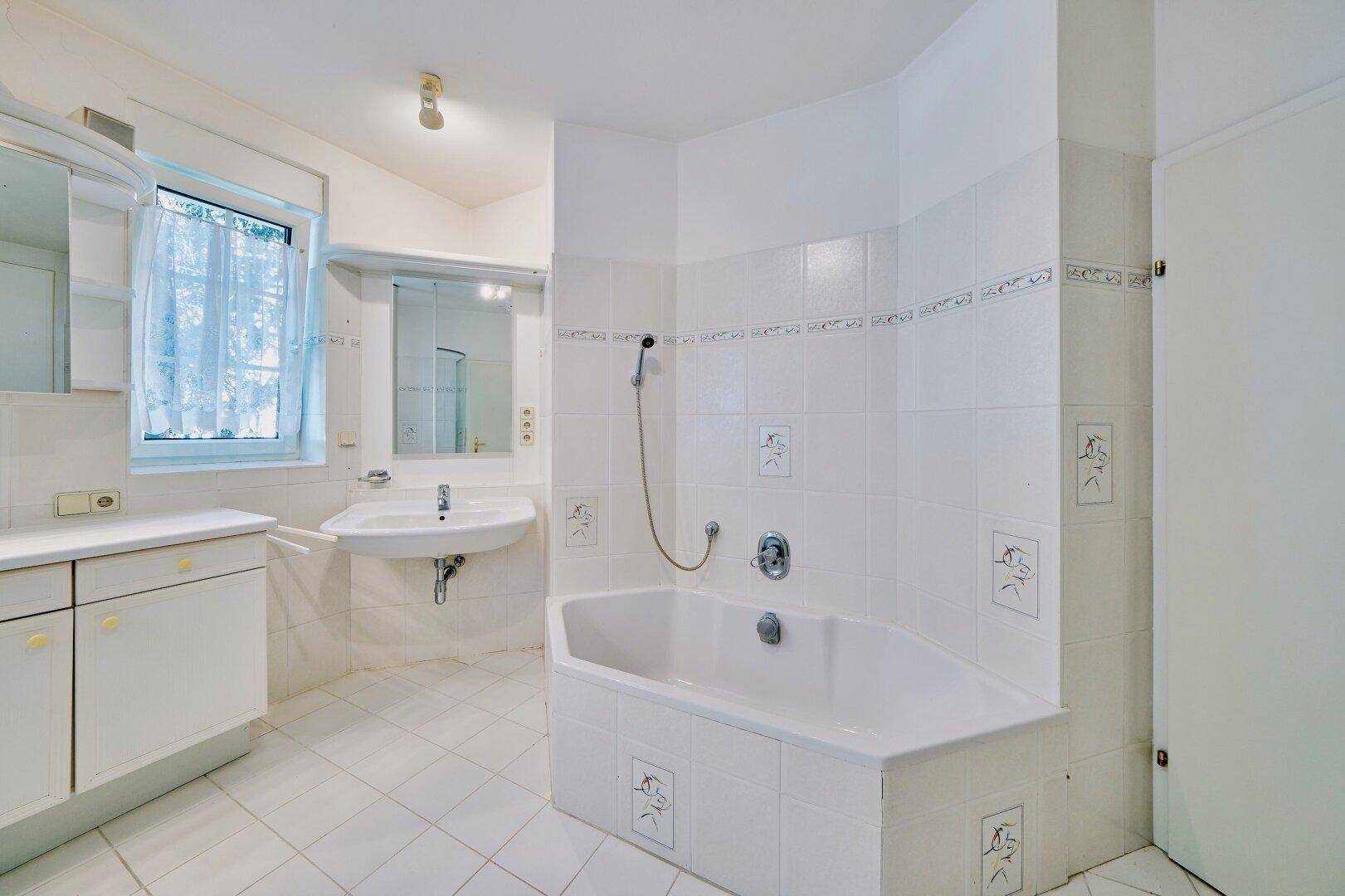 Badezimmer mit Eckbadewanne, Waschbecken, Spiegelschrank und Fenster für natürliches Tageslicht.