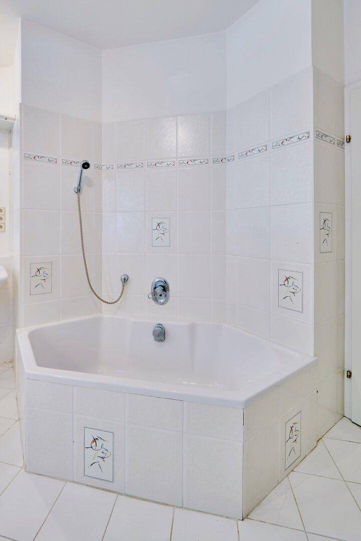 Eckbadewanne in einem hell gefliesten Badezimmer mit dekorativen Akzenten.