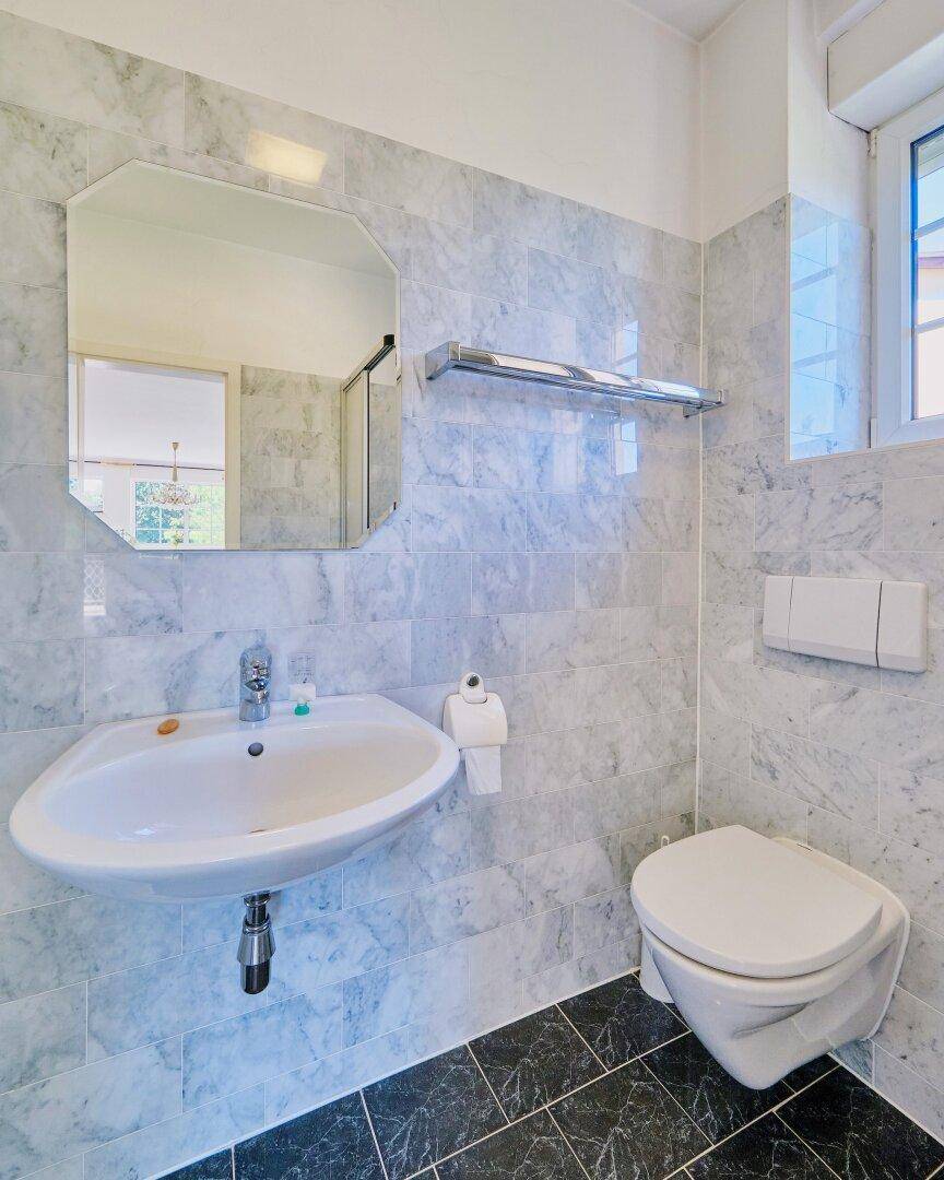 Helles Gäste-WC mit Marmorfliesen, Waschbecken und wandhängender Toilette.