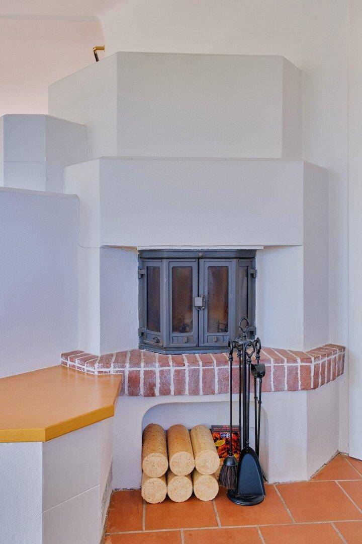 Gemütlicher Kaminofen mit Ziegeldetails und Holzscheiten, umgeben von Terrakottafliesen.