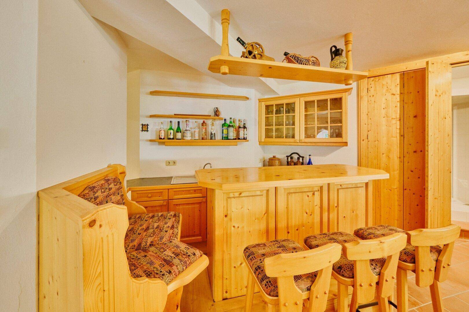 Rustikaler Barbereich mit Holztheke, Hockern und Regalen, ideal für gesellige Abende.