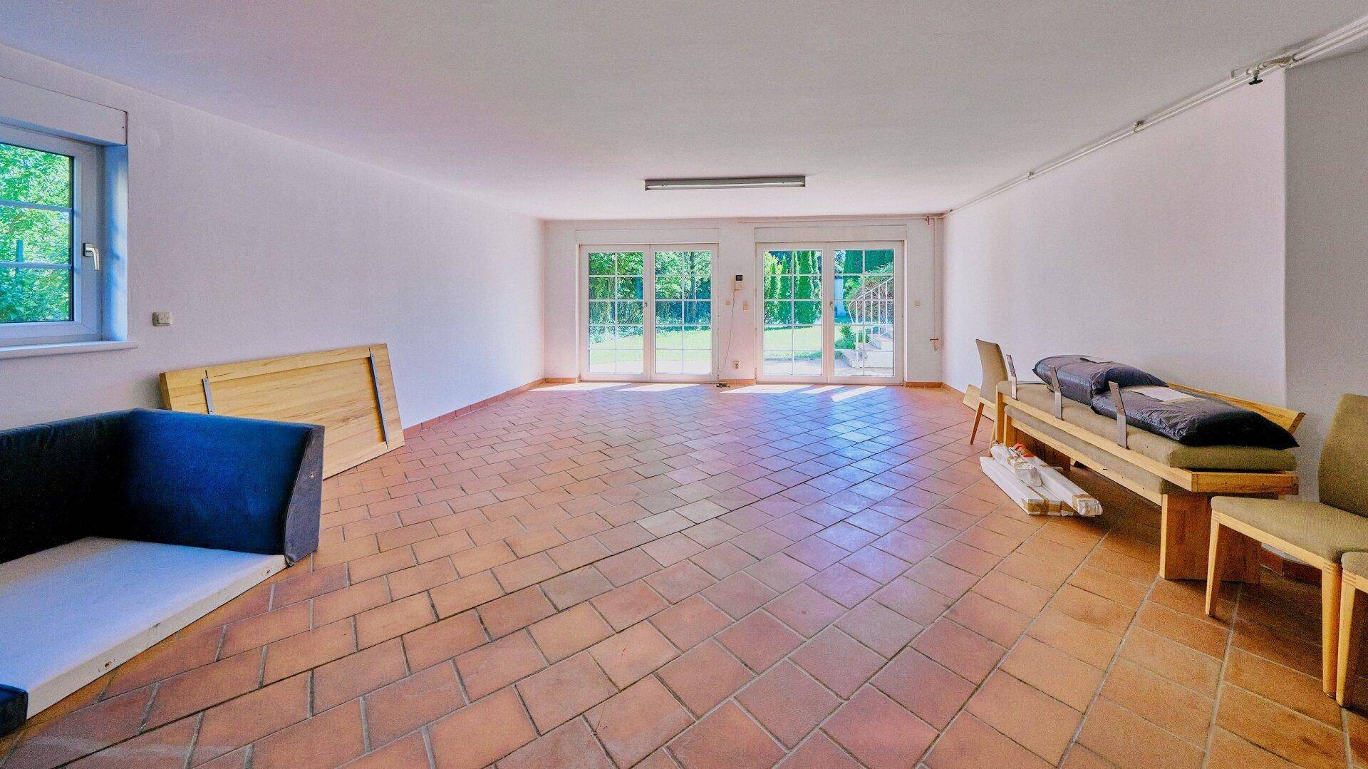 Heller Wohnraum mit Terrakottafliesen und großen Fenstertüren zum Garten.