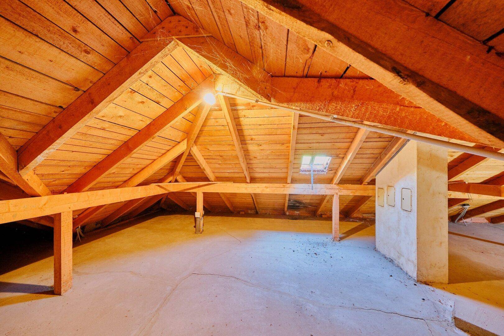 Heller Dachboden mit Holzbalken und einem kleinen Dachfenster, das Licht hereinlässt.