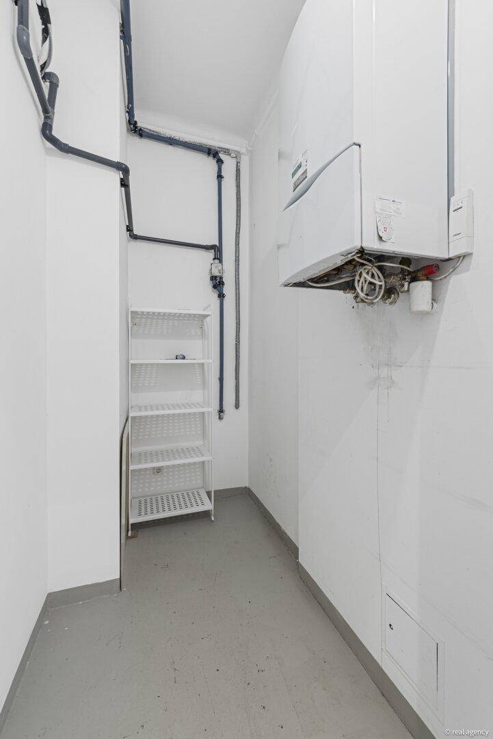 Kleiner Hauswirtschaftsraum mit Gastherme, Rohren und einem einfachen Regal.
