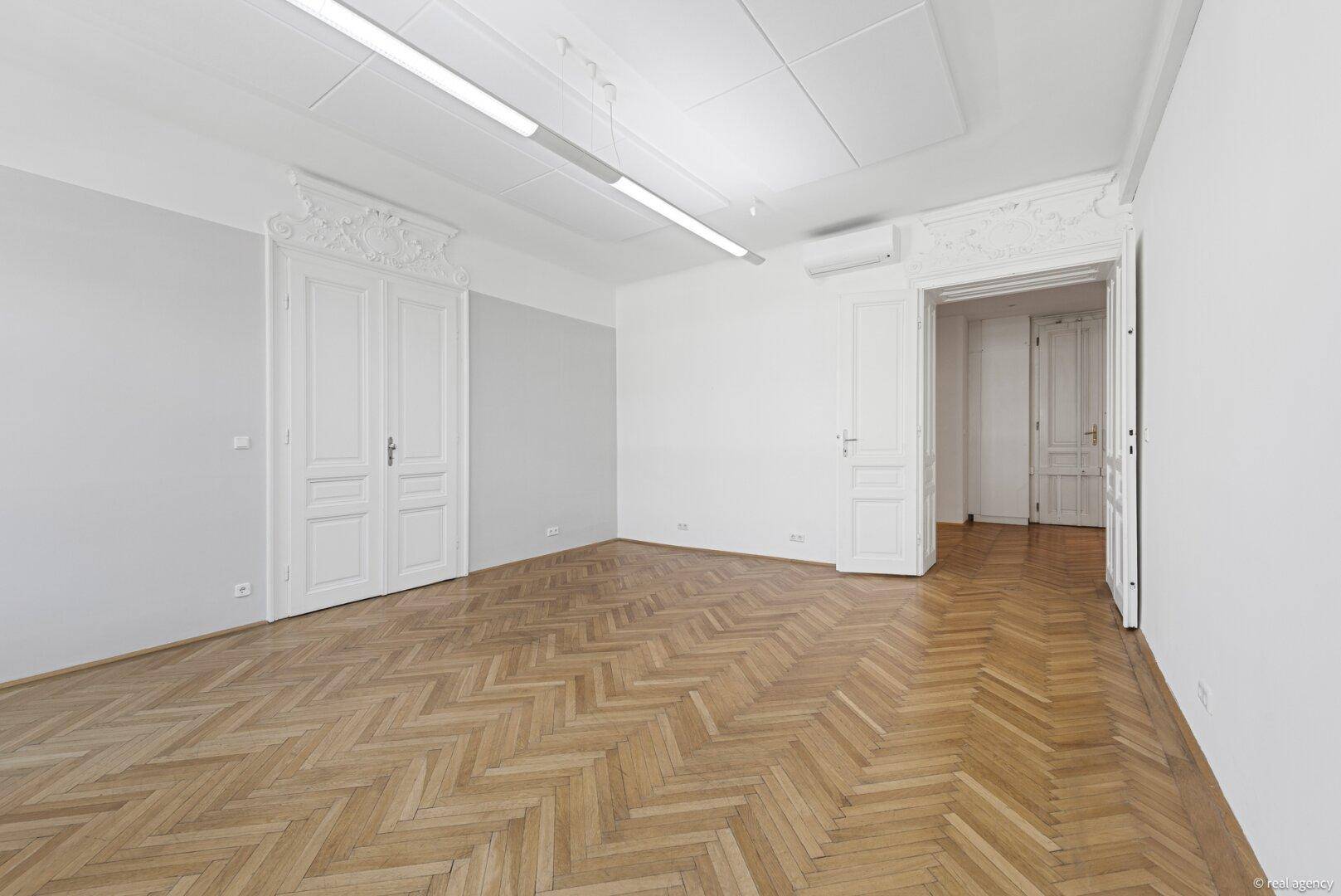 Heller Raum mit Fischgrätparkett, dekorativen Türen und Klimaanlage, ideal für Büro.