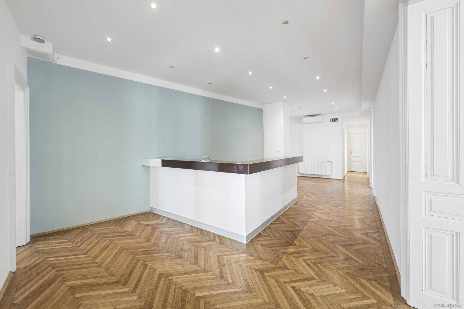 Empfangsbereich mit moderner Theke, Fischgrätparkett und hellblauer Akzentwand.