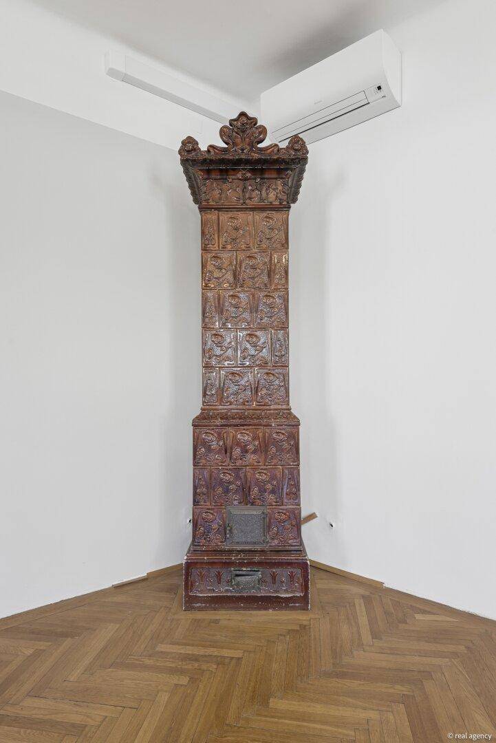 Detailansicht eines historischen Kachelofens mit kunstvollen Verzierungen in einem hellen Raum.