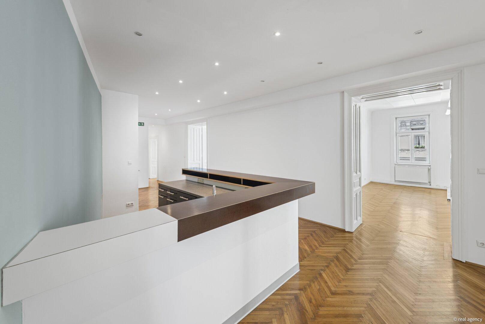 Empfangsbereich mit moderner Theke, Fischgrätparkett und Blick in angrenzende Räume.