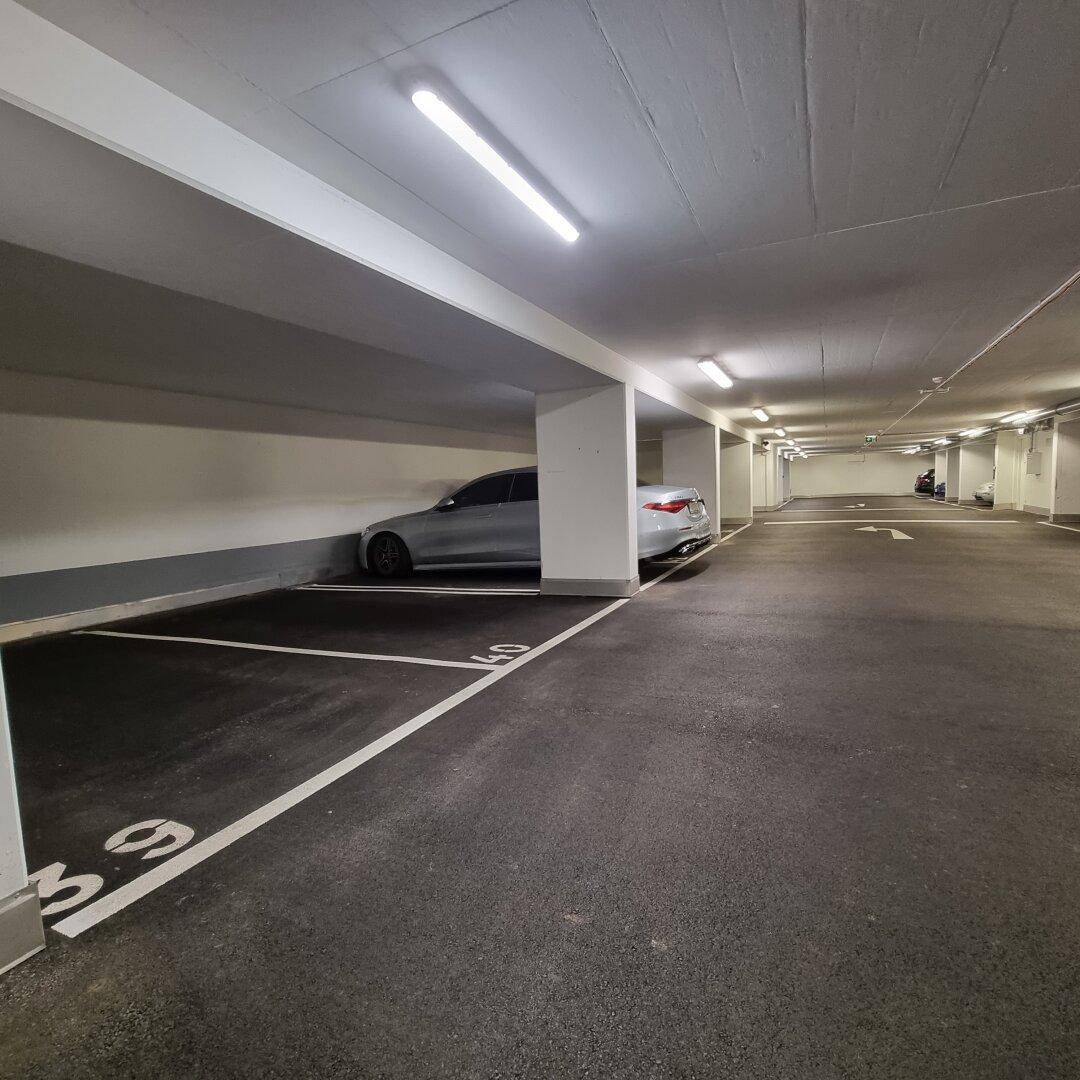 Geräumige und gut beleuchtete Tiefgarage mit markierten Stellplätzen und einem geparkten Fahrzeug.